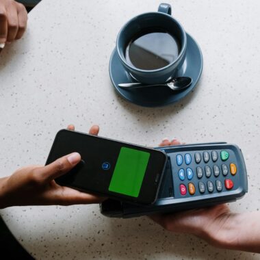 Contactless payment using a smartphone and card reader at a coffee shop table.